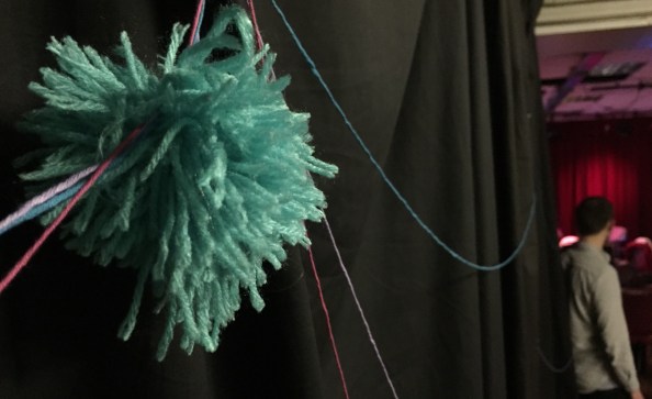 A fluffy handmade cancer cell attached to the threads of clinical trials stories disappearing into the theatre